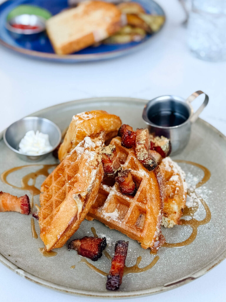 A decadent stack of smoked-bacon-stuffed Belgian waffles topped with slow-roasted bacon lardons, salted caramel, a shimmer of gold dust, and a pour of Québec maple syrup.